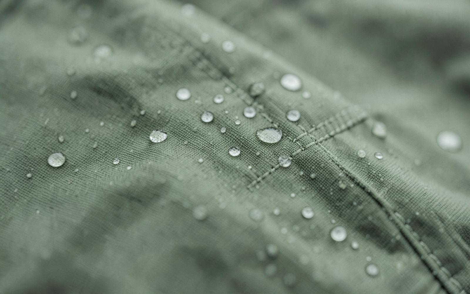 Water droplets beading on the taut ripstop face fabric of a waterproof jacket beside a taped seam